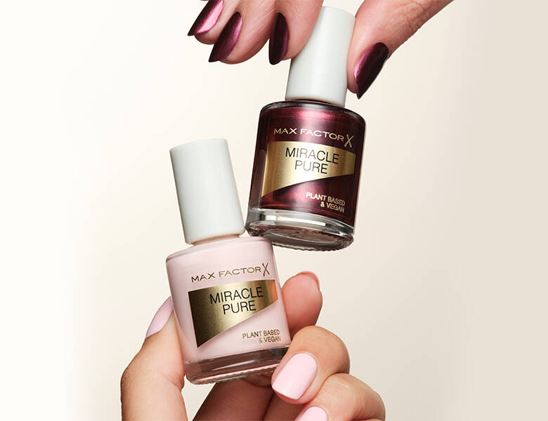 Her ses to neglelakker fra Max Factor. Baggrunden er hvid og de to neglelakker holdes af to hænder.