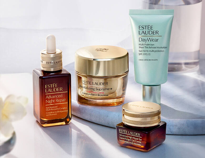 Her ses fire Estée Lauder produkter stående på et lyst stenfad med en lys baggrund.