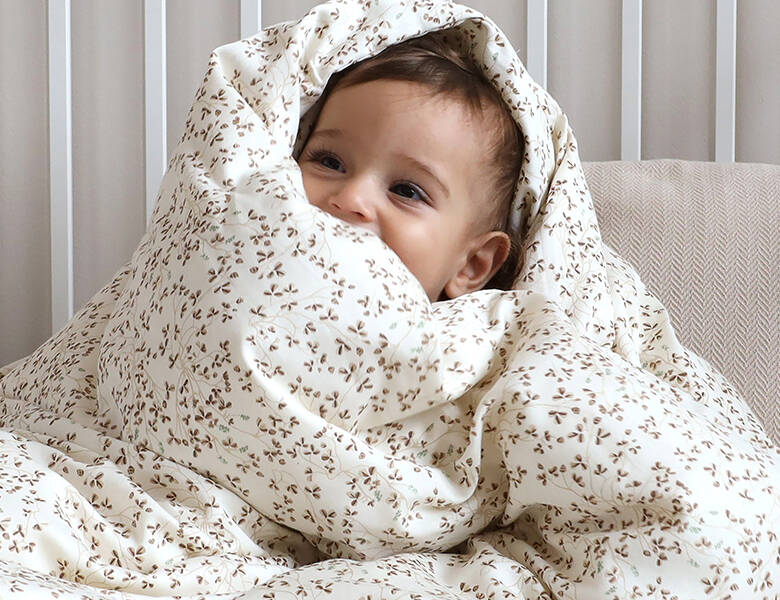 Baby kigger frem fra en lys blomstret dyne i et blødt og roligt miljø.