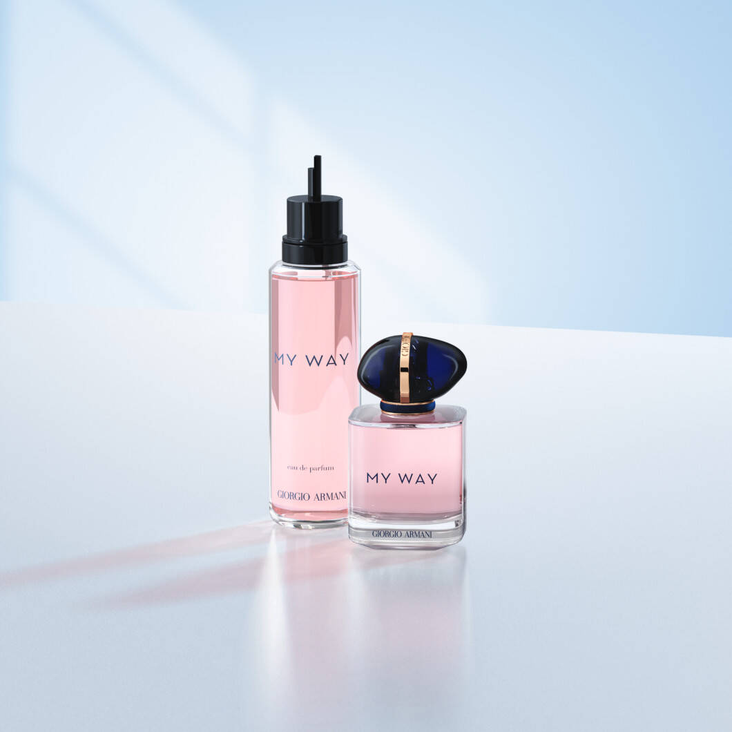 To Giorgio Armani My Way-parfumeprodukter står på en lys overflade foran en blød lyseblå baggrund. Til venstre ses en høj refillflaske med lyserød parfume og sort pumpe. Til højre står den originale My Way-parfumeflaske med mørkeblåt låg og gulddetaljer. Billedet har et elegant og moderne udtryk med fokus på luksusparfume og refill-løsninger.