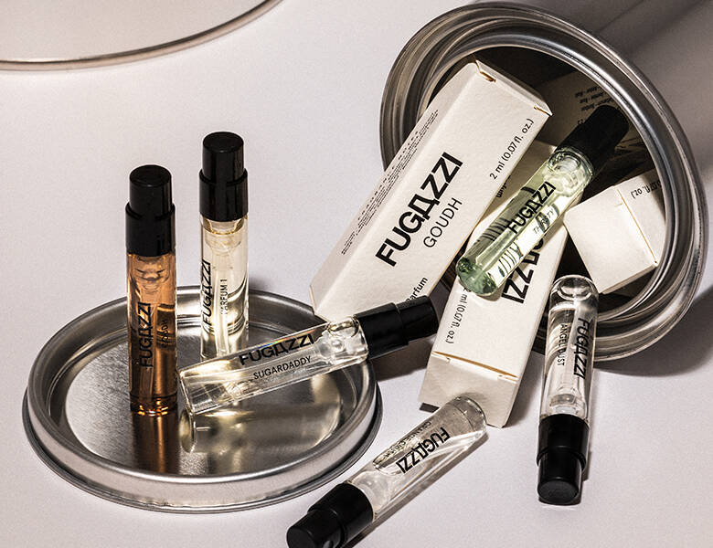 Her ses en hvid baggrund med mange små Fugazzi parfumer. De vælter ud af en metaldåse.