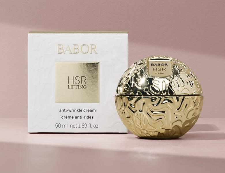 Her ses en lyserød baggrund med et stort guld produkt fra Babor. 