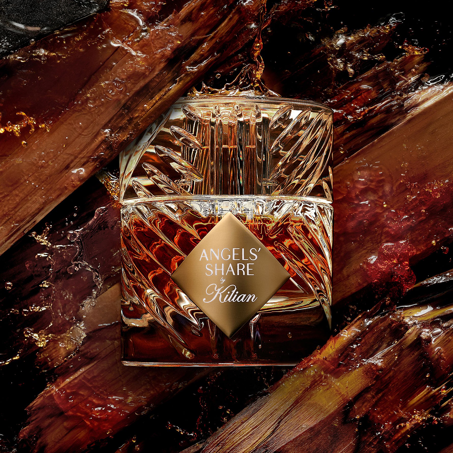 Her ses et billede af en parfumeflakon fra Kilian placeret centralt mod en mørk baggrund. På flakonen står teksten “OLD FASHIONED by Kilian”. Flakonen har et facetteret design i klare og gyldne nuancer og er omgivet af træstykker og små partikler.