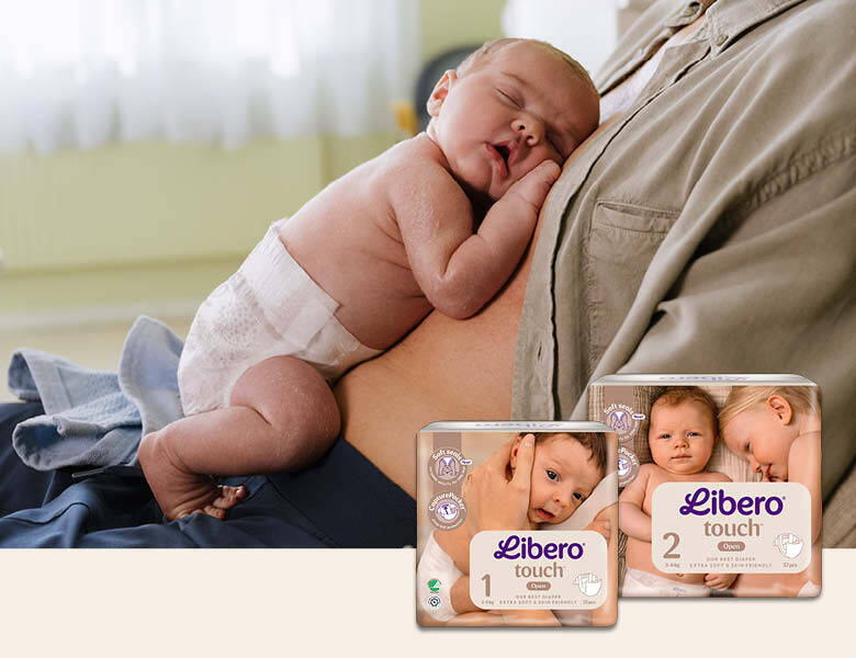 Her ses en lille sovende nyfødt på en fars mave. I nederste højre hjørne ses to slags Libero bleer.