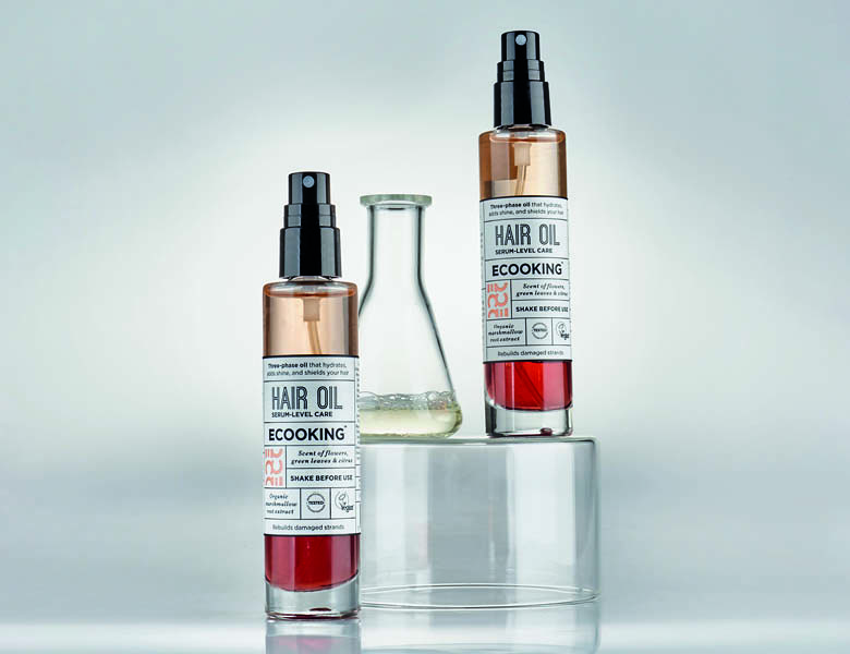 Her ses en hånd, som holder et beige Ecooking produkt. Baggrunden er et badekar fyldt med skum.