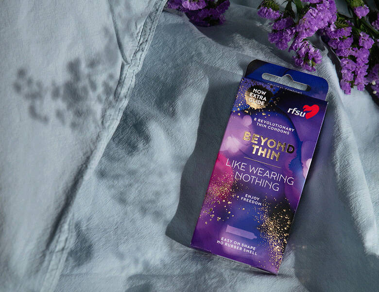 Her ses en lilla pakke kondomer i en grå seng.