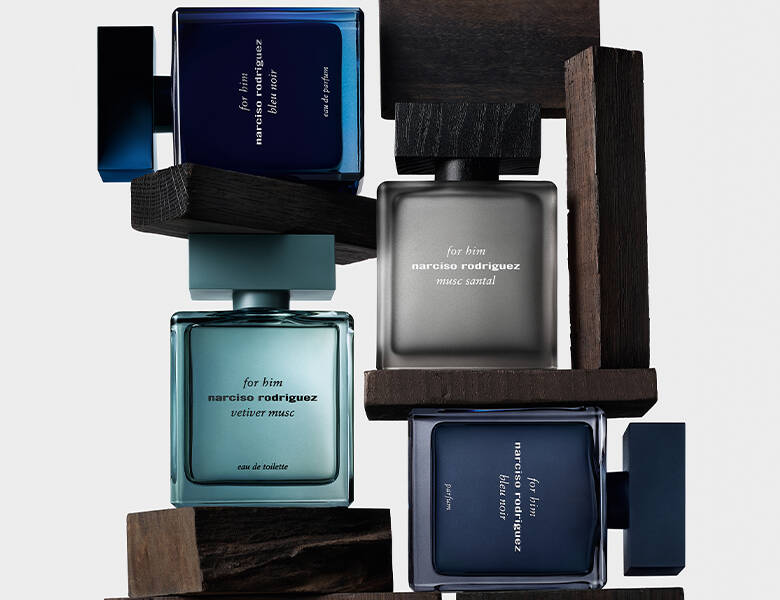 Her ses et billede med flere parfumeflakoner fra narciso rodriguez placeret i en opbygget struktur af mørke træelementer mod en lys baggrund. Flakonerne er i nuancer af blå, grå og grøn, og på dem står teksten “for him narciso rodriguez” samt varianter som “vetiver musc”, “musc santal” og “bleu noir”.