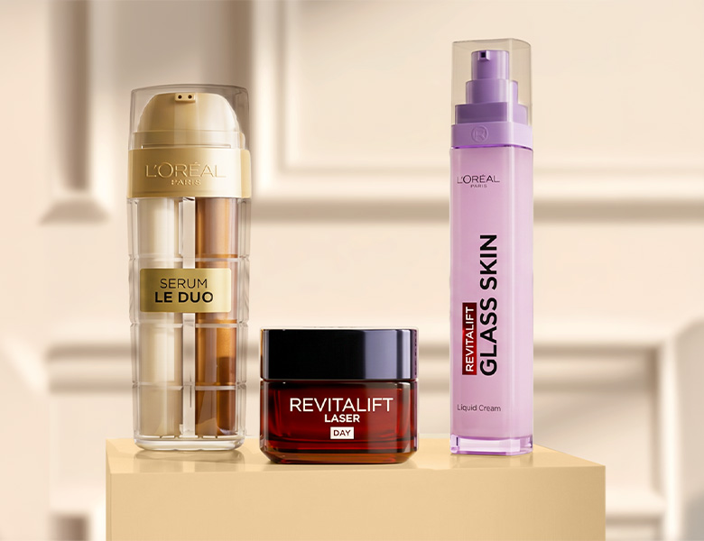 Her ses tre L’Oréal Paris hudplejeprodukter på en beige sokkel: Serum Le Duo, Revitalift Laser Day Cream og Revitalift Glass Skin Liquid Cream.