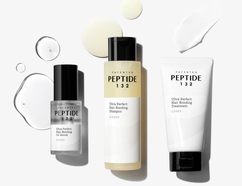 Her ses et billede med tre hårplejeprodukter fra COSRX placeret mod en lys baggrund. På produkterne står teksten “PEPTIDE 132” samt “Ultra Perfect Hair Bonding Oil Serum”, “Shampoo” og “Treatment”. Produkterne er i klare, beige og hvide emballager med sorte låg.