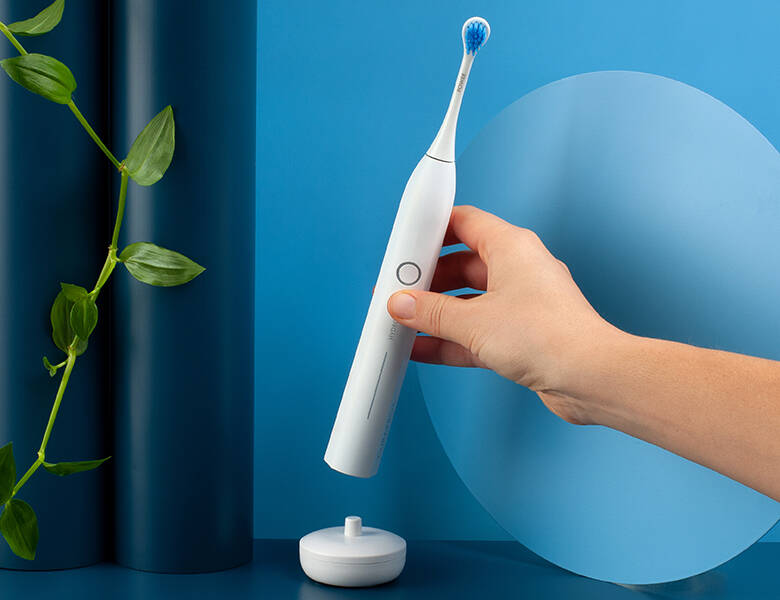 Her ses en hånd, som holder en elektrisk tandbørste i hvid. Baggrunden er blå.