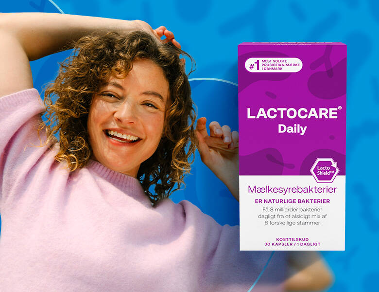 Kvinde med mørkt krøllet hår i lyserød strik ligger på en blå baggrund. Der ses Lactocare Daily pakke i forggrunden