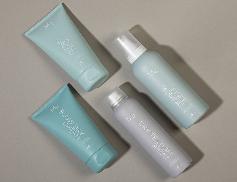 Her ses fire forskellige IdHAIR produkter i blå nuancer på en grå baggrund. 