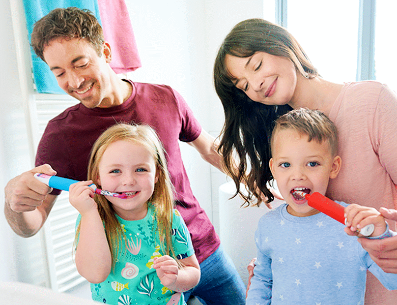 Her ses en mor og en far, som hver børster tænder på en af deres børn. Alle fire ser glade ud. 