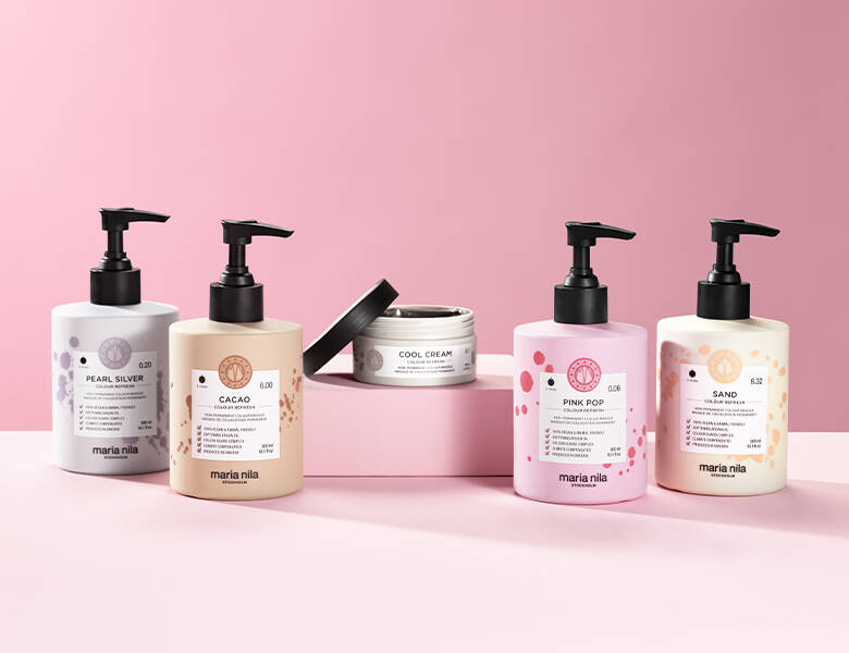 Her ses en lyserød baggrund med fem forskellige Maria Nila produkter i forskellige farver.