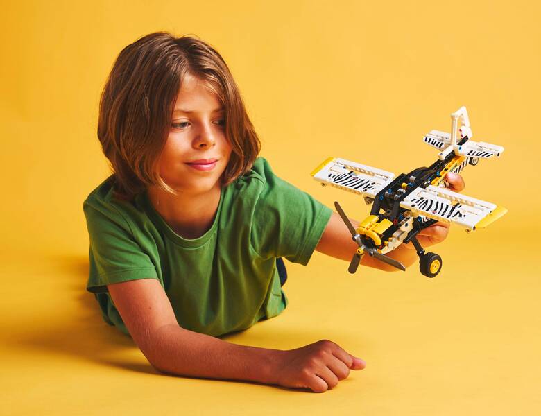 Her ses en gul baggrund med en liggende dreng i grøn trøje. Han holder et legofly. 