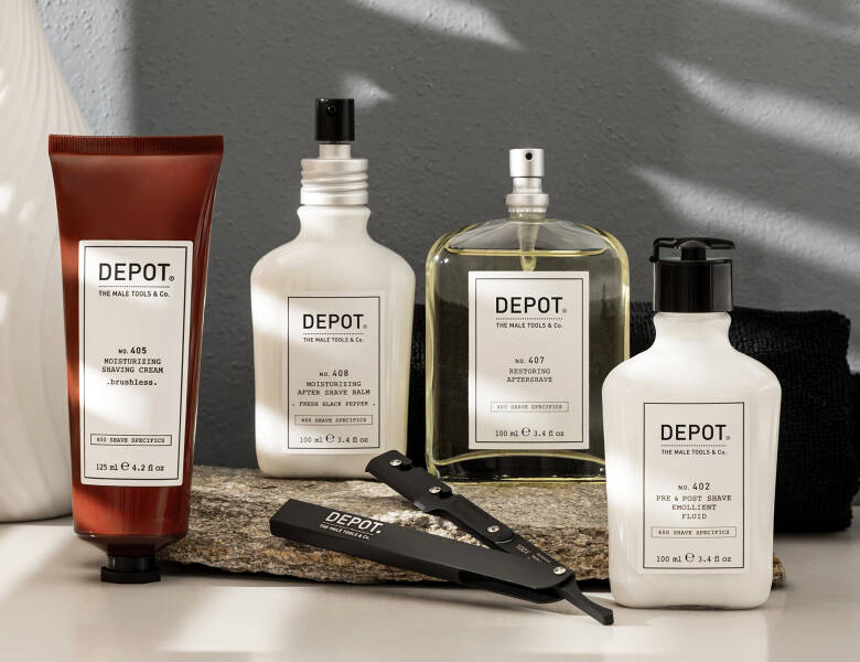 Her ses et billede med flere produkter fra DEPOT placeret på en overflade mod en lys baggrund. På produkterne står blandt andet “DEPOT”, “Moisturizing Shaving Cream”, “After Shave Balm”, “Restoring Aftershave” og “Pre & Post Shave Emollient Fluid”. Der ligger også en barberkniv foran produkterne.
