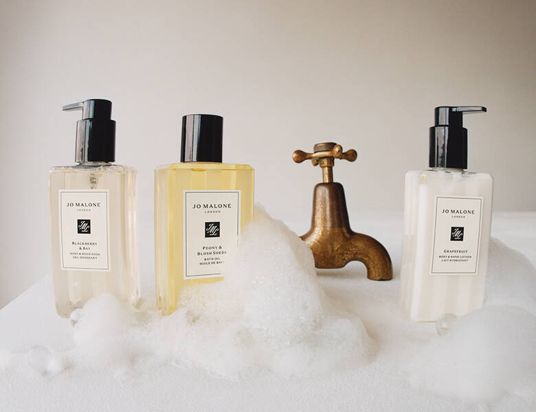 Her ses enden af et badekar, som er fyldt med sæbeskum. For enden er der tre Jo Malone London produkter.