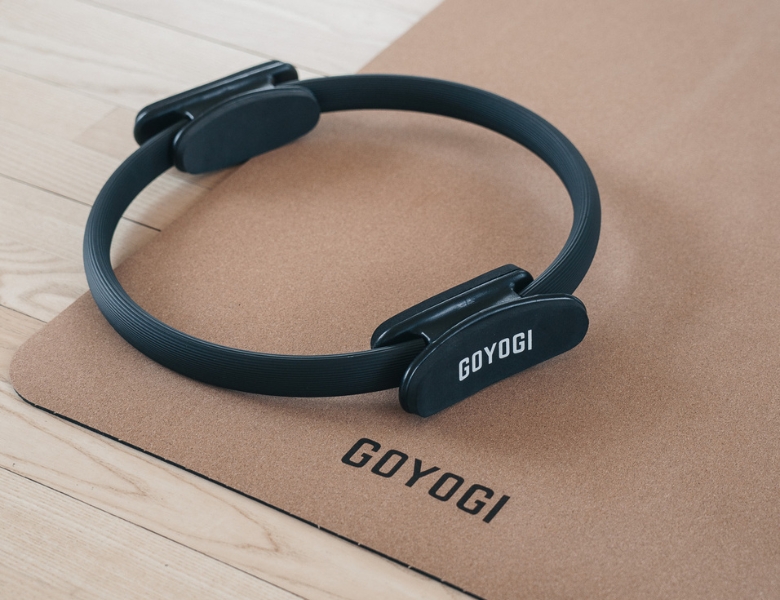 Sort pilatesring ligger på en korkmåtte med GOYOGI-logo på et lyst trægulv.