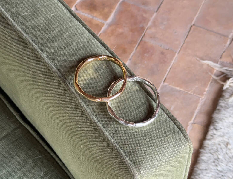 Her ses to armbånd - et i guld og et i sølv. de ligger på en grøn stolkant. 