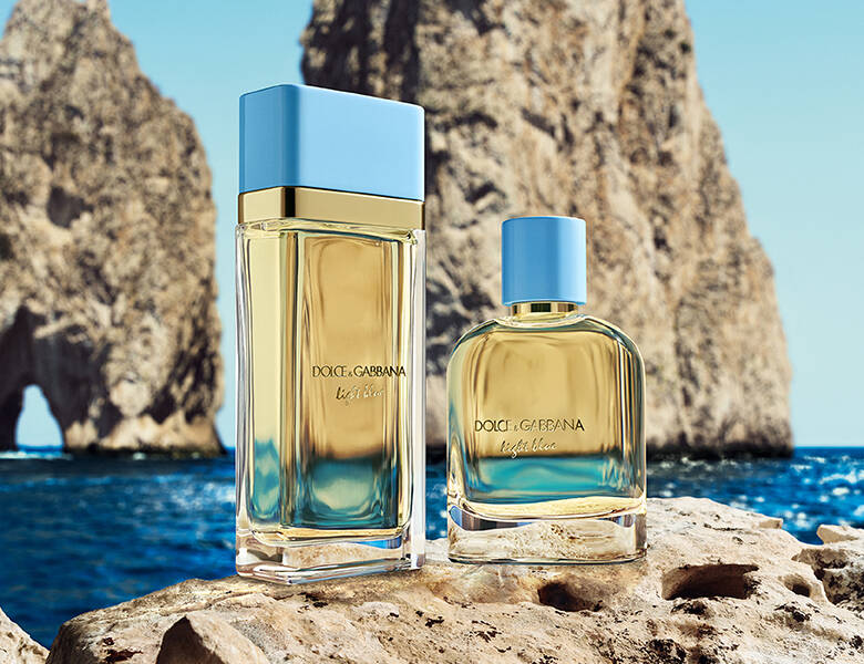 To Dolce & Gabbana Light Blue parfumer med lyseblå låg står på klipper ved havet foran store kystklipper