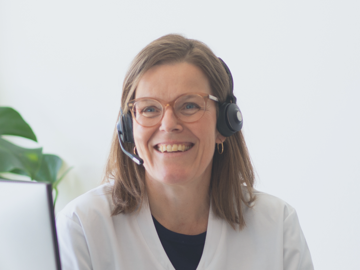 Smilende medarbejder fra Webapoteket med headset sidder ved computer i lyst kontormiljø.