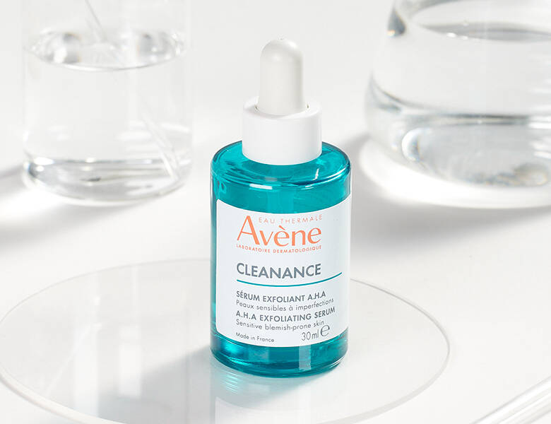 Her ses et Avène produkt i en glasflaske. Baggrunden er lys og har vandglas stående.