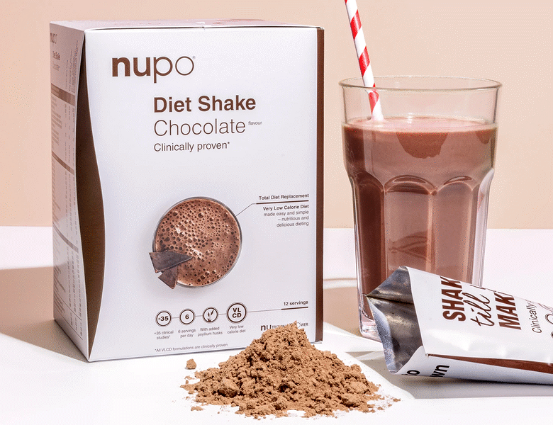 Her ses et Nupo produkt i dets pakke samt et glas, hvor produkt er brugt. Smagen er chocolade og baggrunden er brun og hvid. 