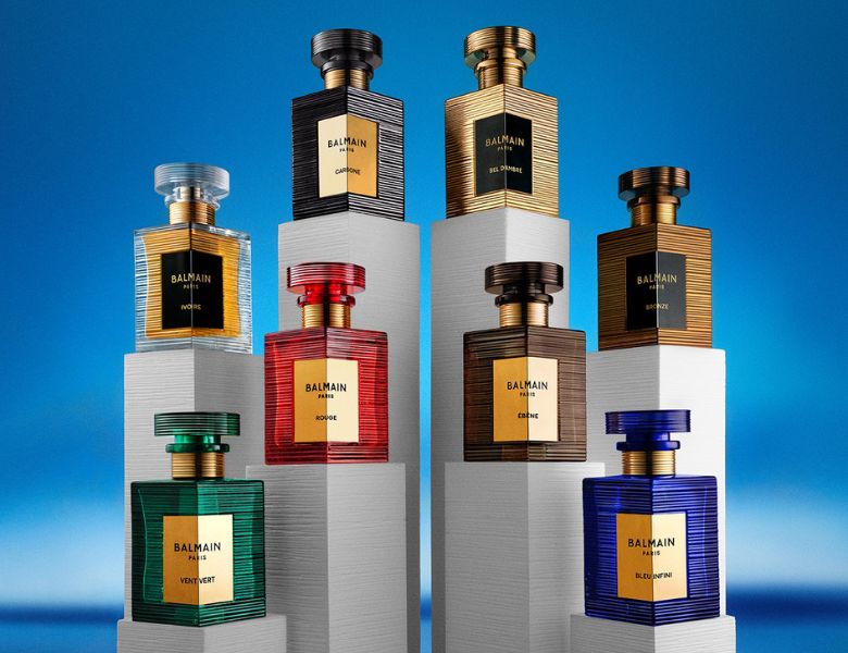 Her ses et billede med flere parfumeflakoner fra Balmain placeret på podier mod en blå baggrund. På flakonerne står teksten “BALMAIN PARIS” samt forskellige varianter. Flakonerne er i forskellige farver som grøn, rød, blå og gyldne nuancer.