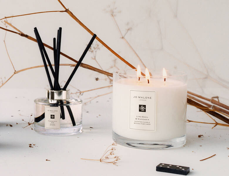 Her ses en hvid baggrund med et Jo Malone London duftlys og nogle duftpinde. 