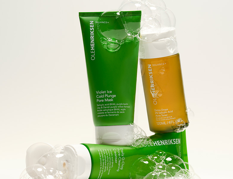 Her ses OLE HENRIKSEN hudplejeprodukter i grøn og transparent emballage på en lys baggrund med skum.