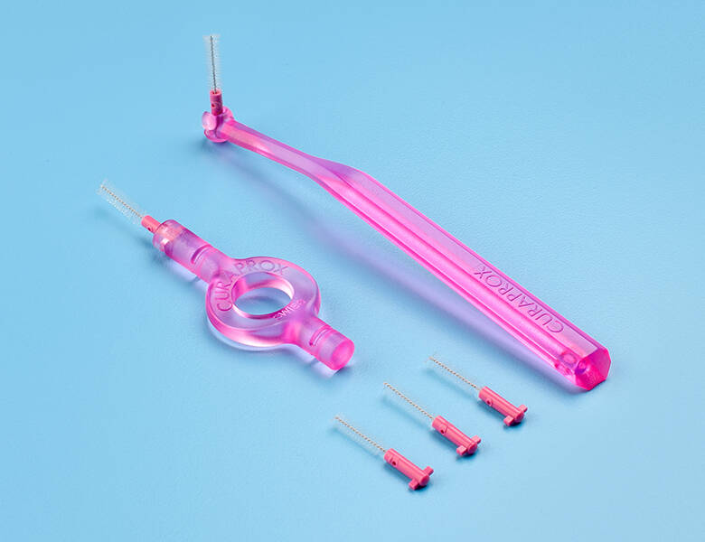 Her ses lyserøde værktøjer til mellemrummene i tænderne. Baggrunden er lyseblå. 