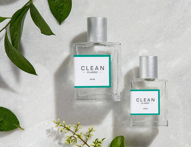 Her ses to Clean parfumer i forskellige størrelser på en hvid baggrund med nogle planter. 