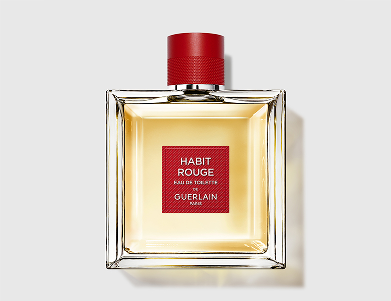 Firkantet Guerlain Habit Rouge parfume i klar glasflaske med rød hætte står centreret på lys grå baggrund.