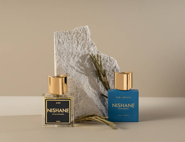 Her ses to NISHANE parfumer foran en sten. Baggrunden er beige.