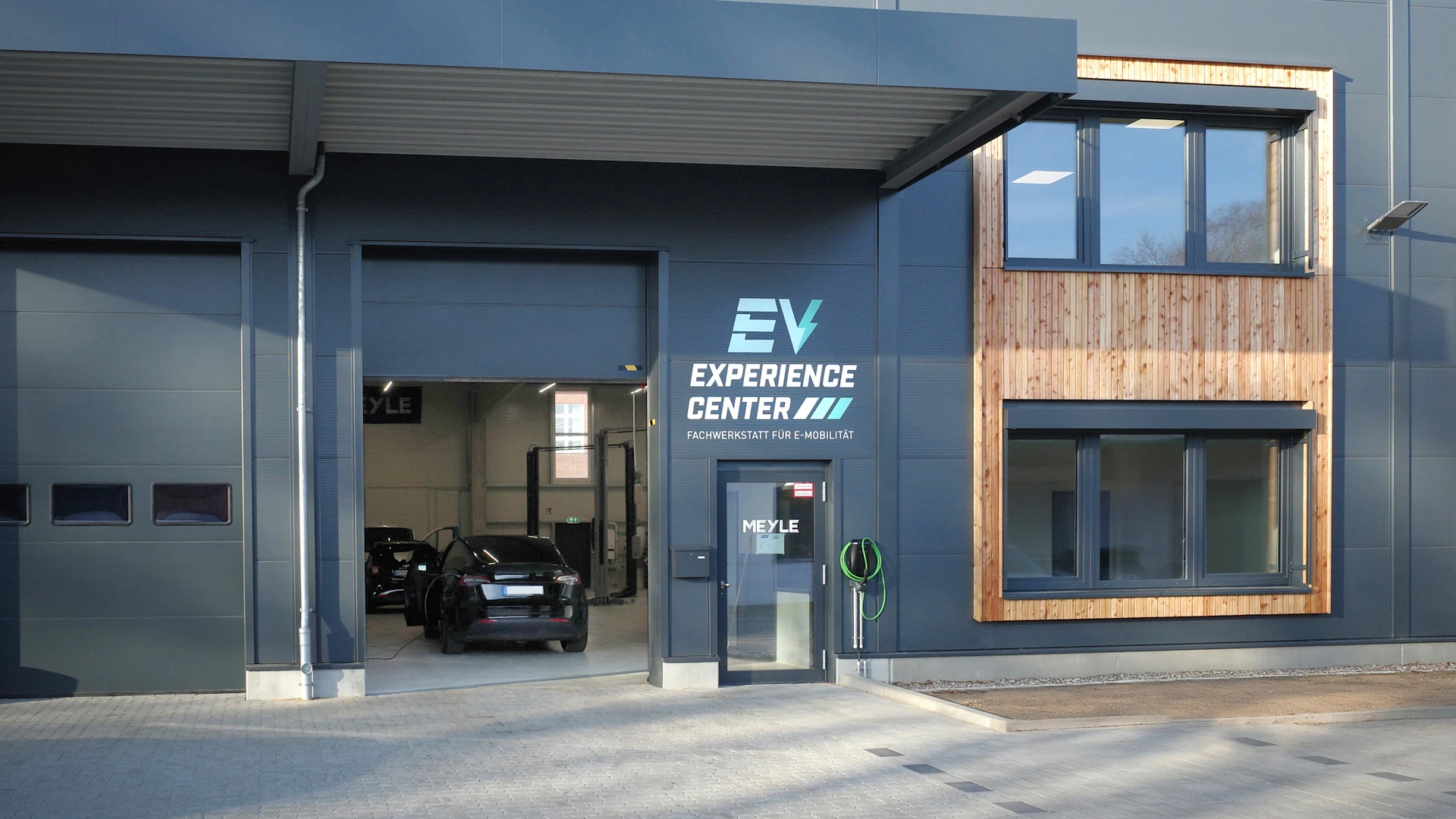 Außenansicht eines Gebäudes mit Einfahrt und Beschilderung zum EV Experience Center.