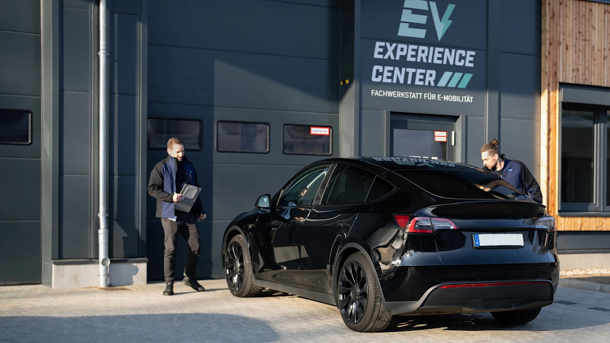 Elektrofahrzeug steht vor einem Gebäude, während Fachpersonal Sicht- und Prüfmaßnahmen im Zusammenhang mit Elektromobilität durchführt.