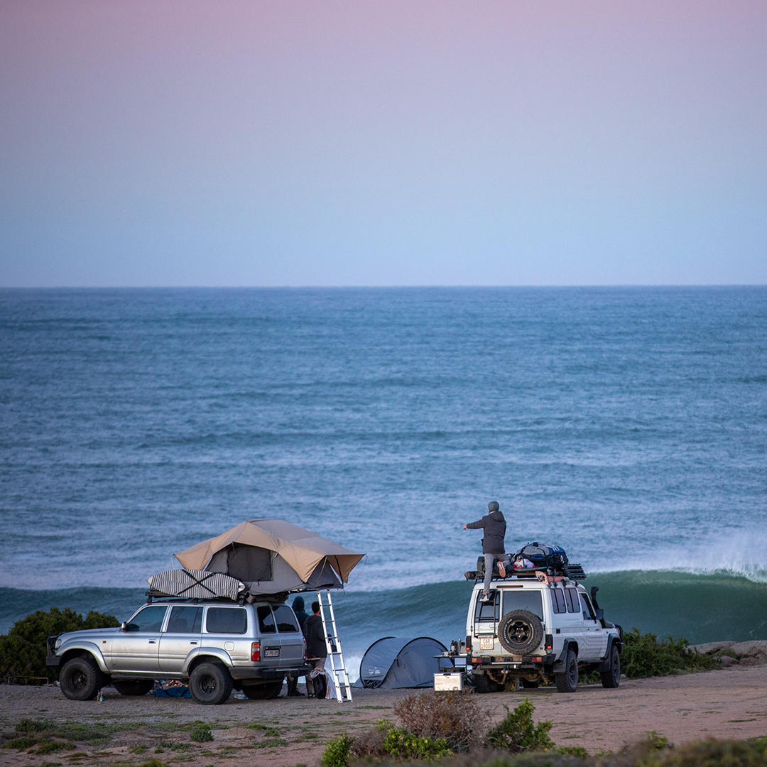 two SUVs at the beach, looking over the surf.