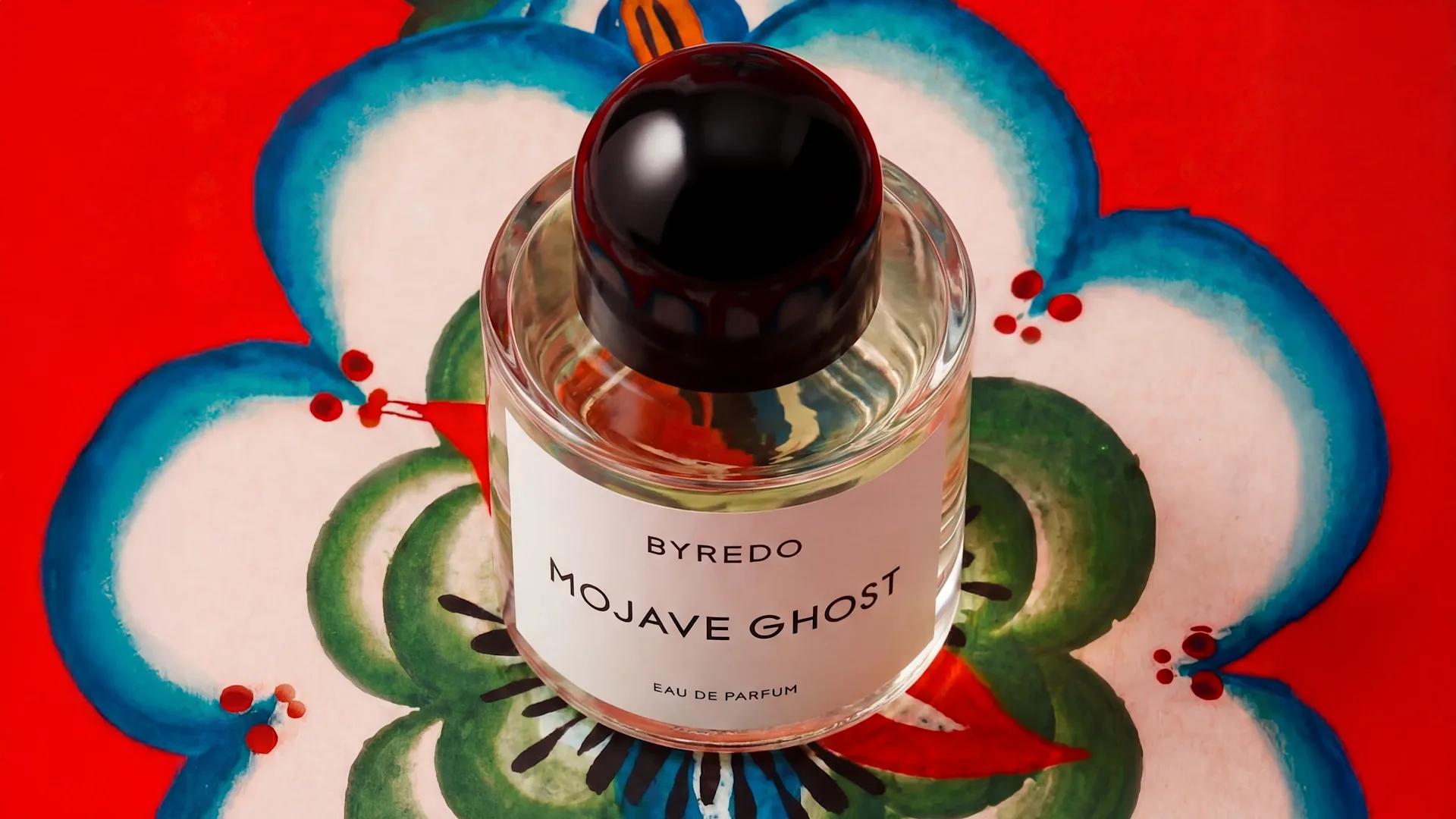 Top view of the Byredo Mojave Ghost Eau de Parfum bottle placed on a hand painted floral motif with a red background