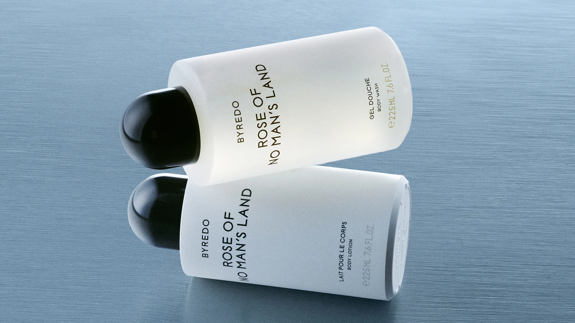 Byredo Rose of No Man’s Land body wash and body lotion bottles placed horizontally on a light blue textured surface