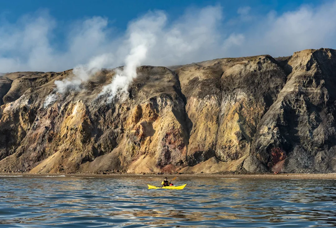 Person in yellow kayak in front of smoking hills.
