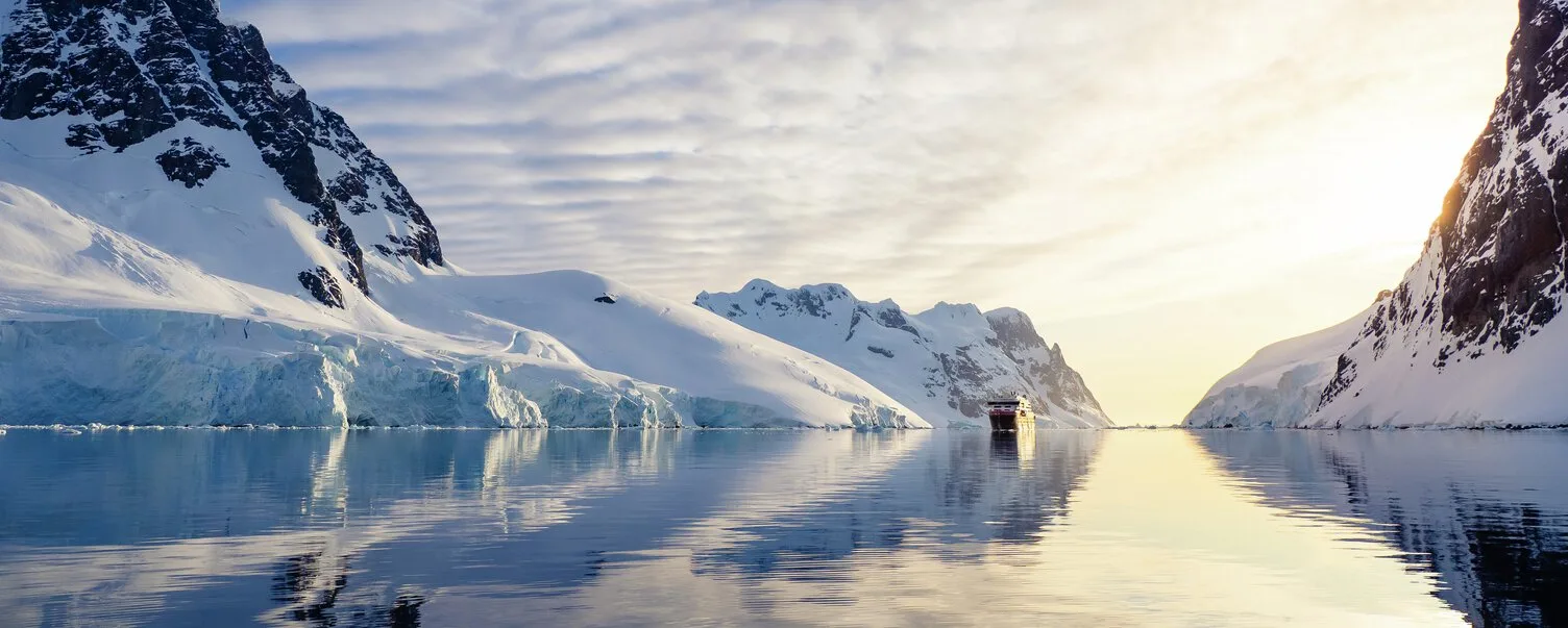 MS Roald Amundsen sailing through the breathtaking Lemaire Channel in Antarctica surrounded by snow-covered mountains. Credit: Espen Mills / HX Hurtigruten Expeditions