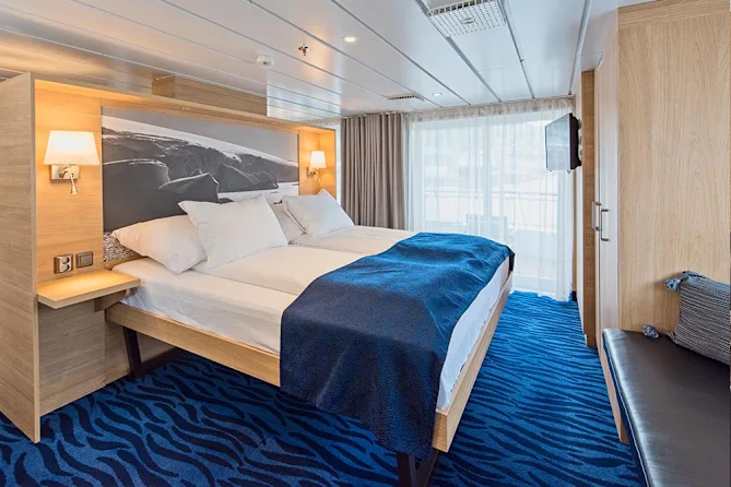 Suite moderna y luminosa a bordo de un barco de expedición HX Hurtigruten, con grandes ventanales y vistas al paisaje polar.