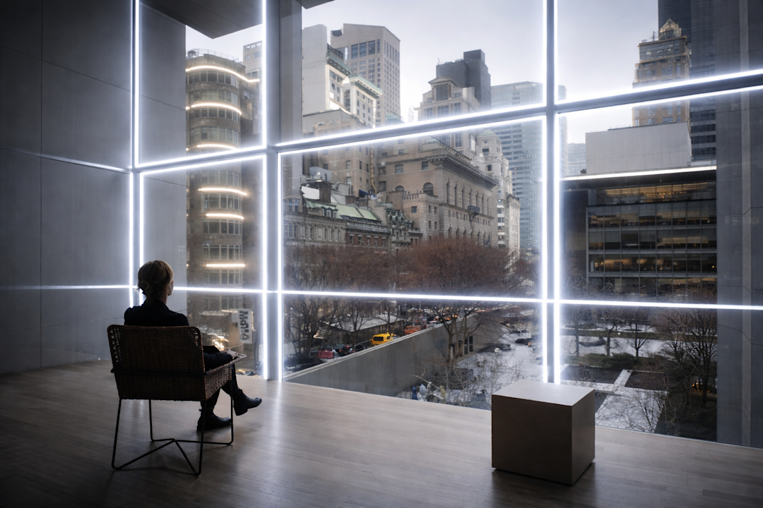 Alt text: Person seated in front of a large window framed by illuminated grid lines symbolizing structured system architecture.