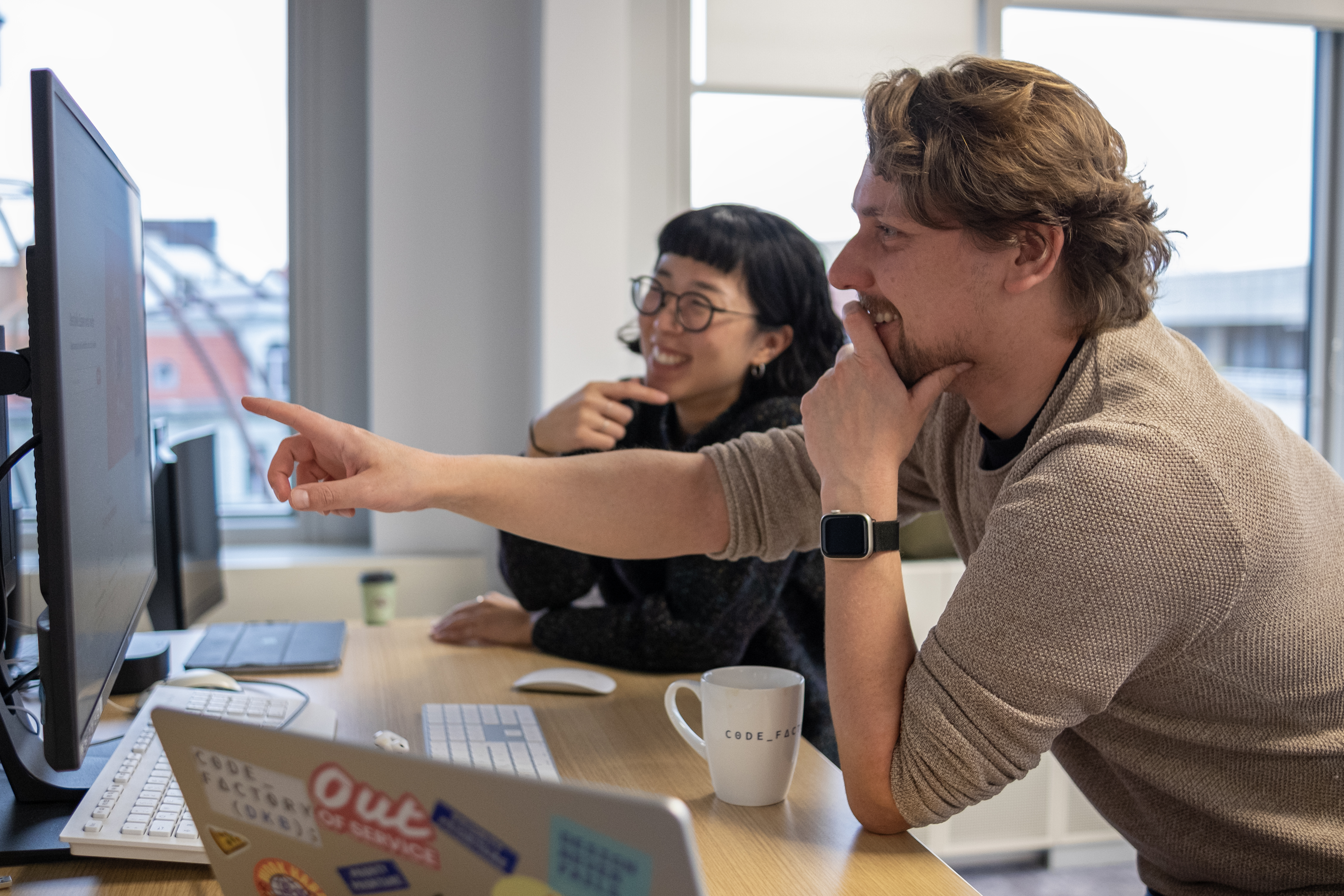 Two designers discussing their work in front of laptops and screens.