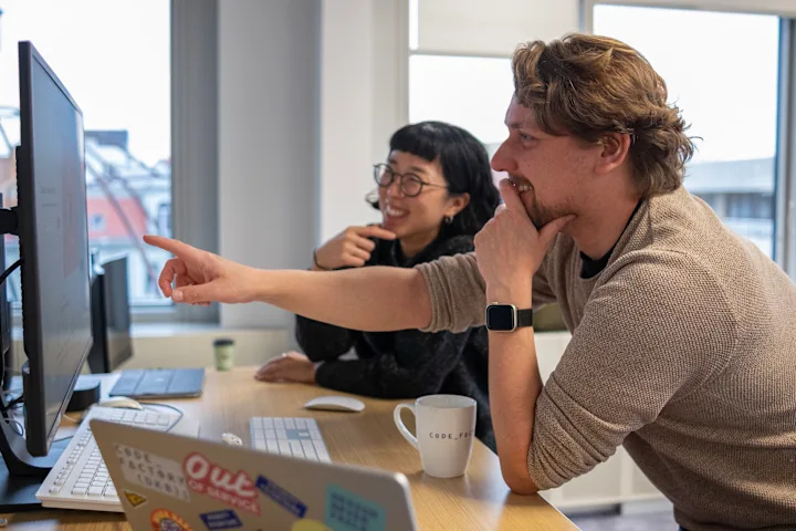 Two designers discussing their work in front of laptops and screens.