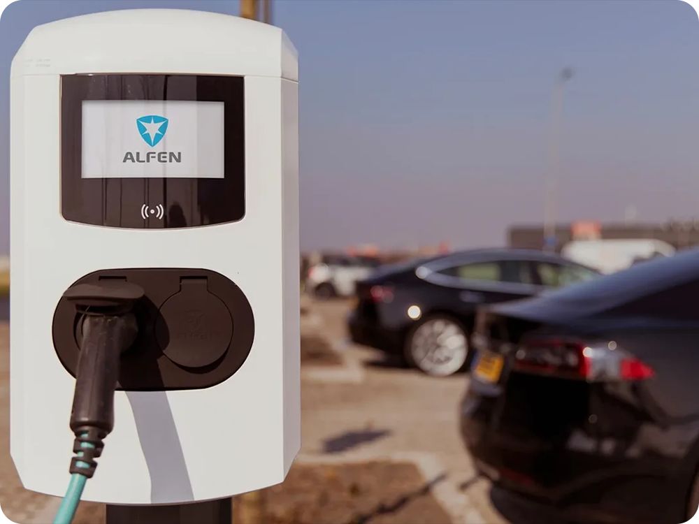 Een Alfen laadpaal op een open terrein, op de achtergrond zie je meerdere auto's naast elkaar