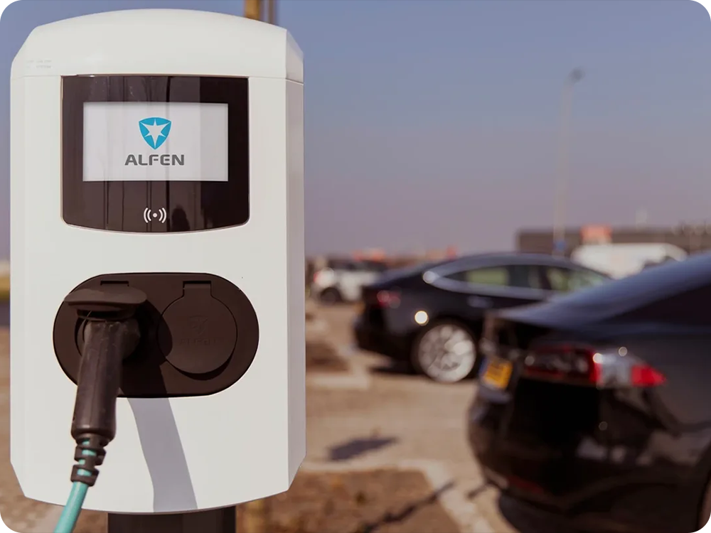 Een Alfen laadpaal op een open terrein, op de achtergrond zie je meerdere auto's naast elkaar
