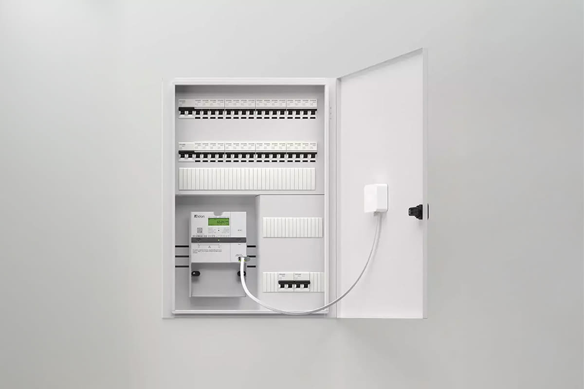 Open elektrische verdeelkast met verschillende installatieautomaten en schakelaars die netjes zijn opgesteld. Een apparaat met een klein scherm, de Zaptec Sense-module, die actieve load balancing toepast, is via een kabel aangesloten. De opstelling bevindt zich in een schone, neutrale ruimte.