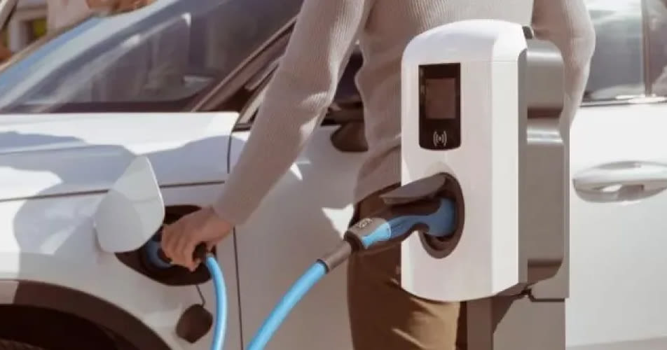 Een persoon die een witte elektrische auto oplaadt bij een Eve Single laadstation, verbonden met een blauwe kabel.