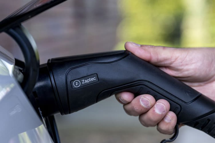 Een hand steekt een zwarte Zaptec oplaadkabel voor elektrische voertuigen in een auto. De afbeelding straalt een gevoel van moderne technologie en duurzaamheid uit.
